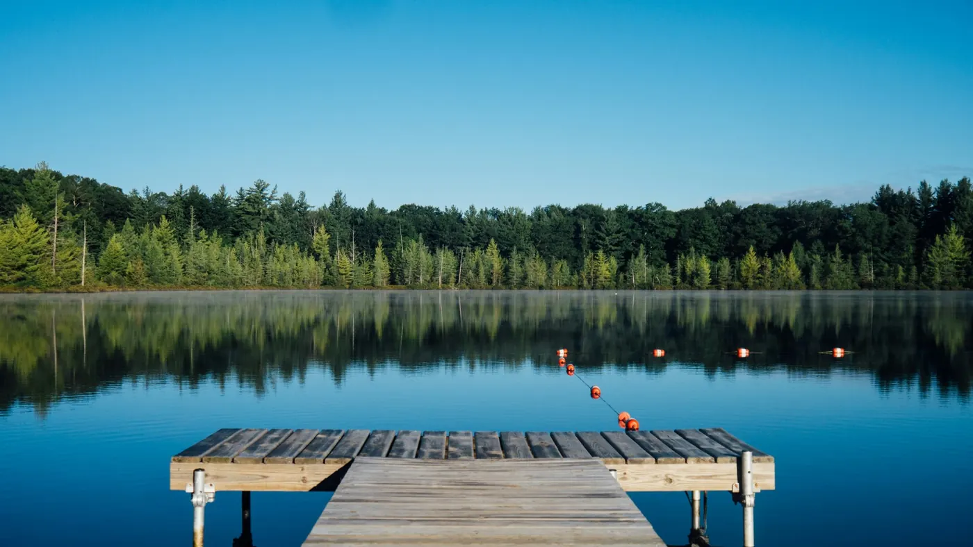 Wooden dock reaching into a calm treelined lake under blue sky, illustrating dock care and permits on Lake Simcoe