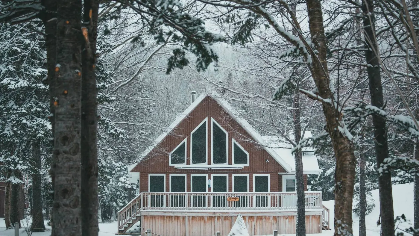 Cottage with large windows and a deck among snow covered trees, illustrating a four season cottage in Muskoka