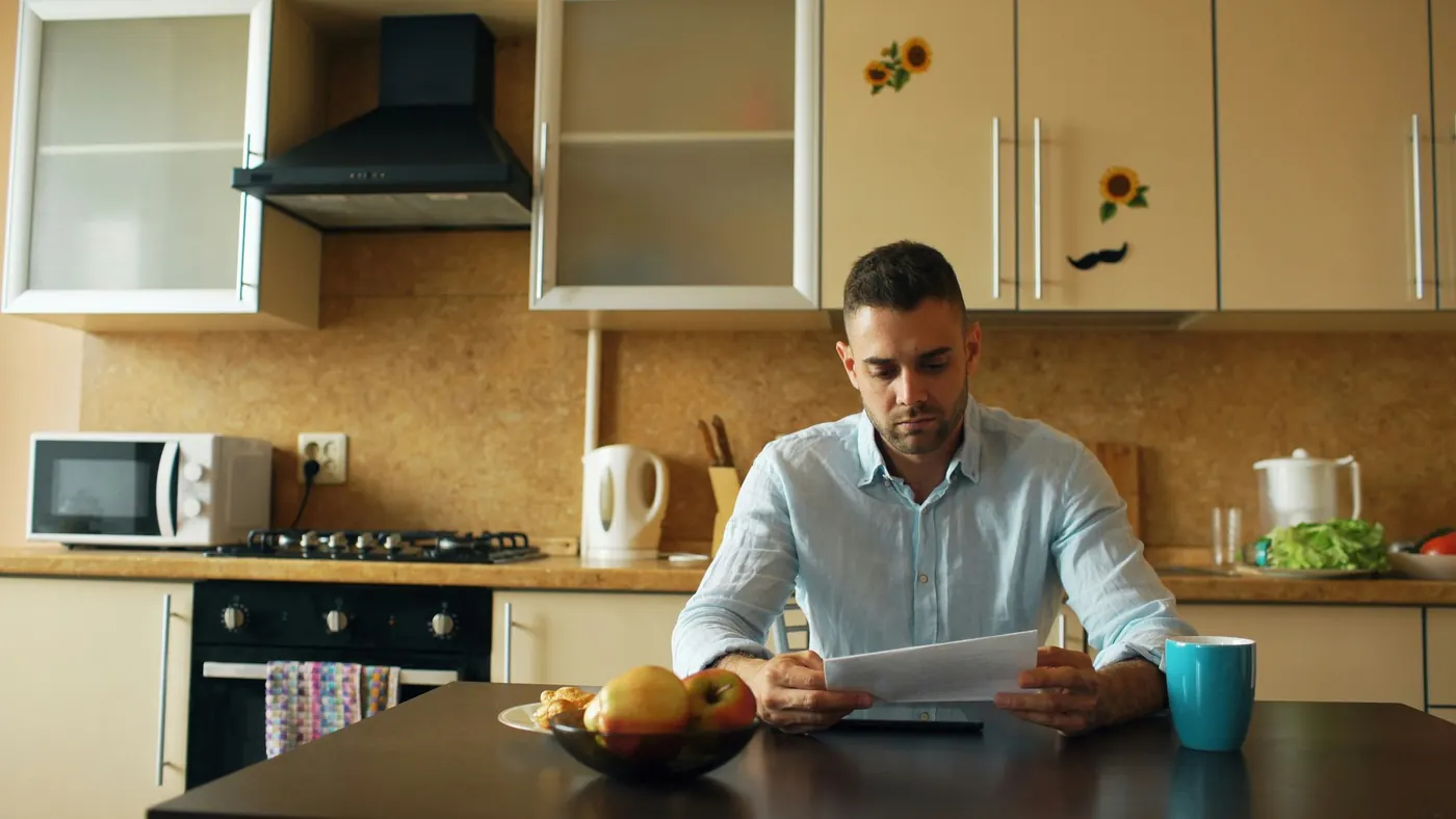 A person reading a document at a kitchen table, illustrating the RECO Information Guide for Ontario consumers