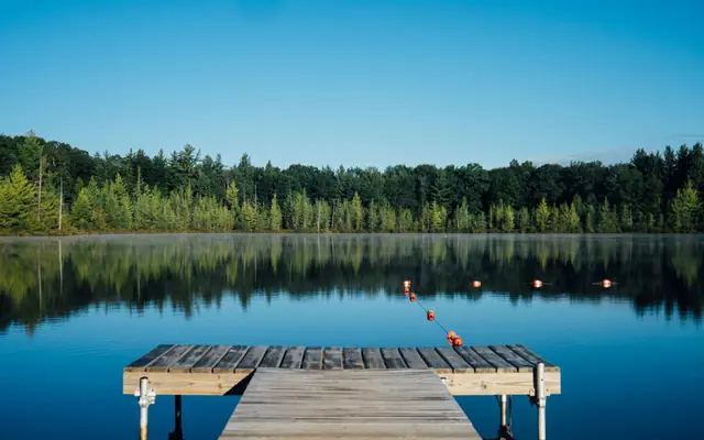 Wooden dock reaching into a calm treelined lake under blue sky, illustrating dock care and permits on Lake Simcoe