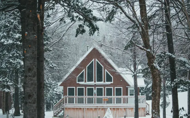 Cottage with large windows and a deck among snow covered trees, illustrating a four season cottage in Muskoka