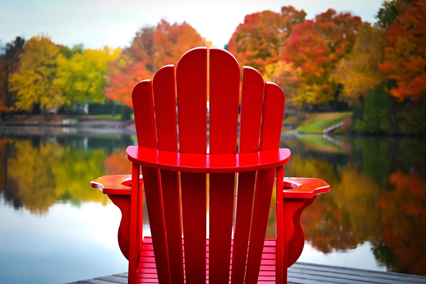 Red Muskoka chair on a dock facing a lake in autumn